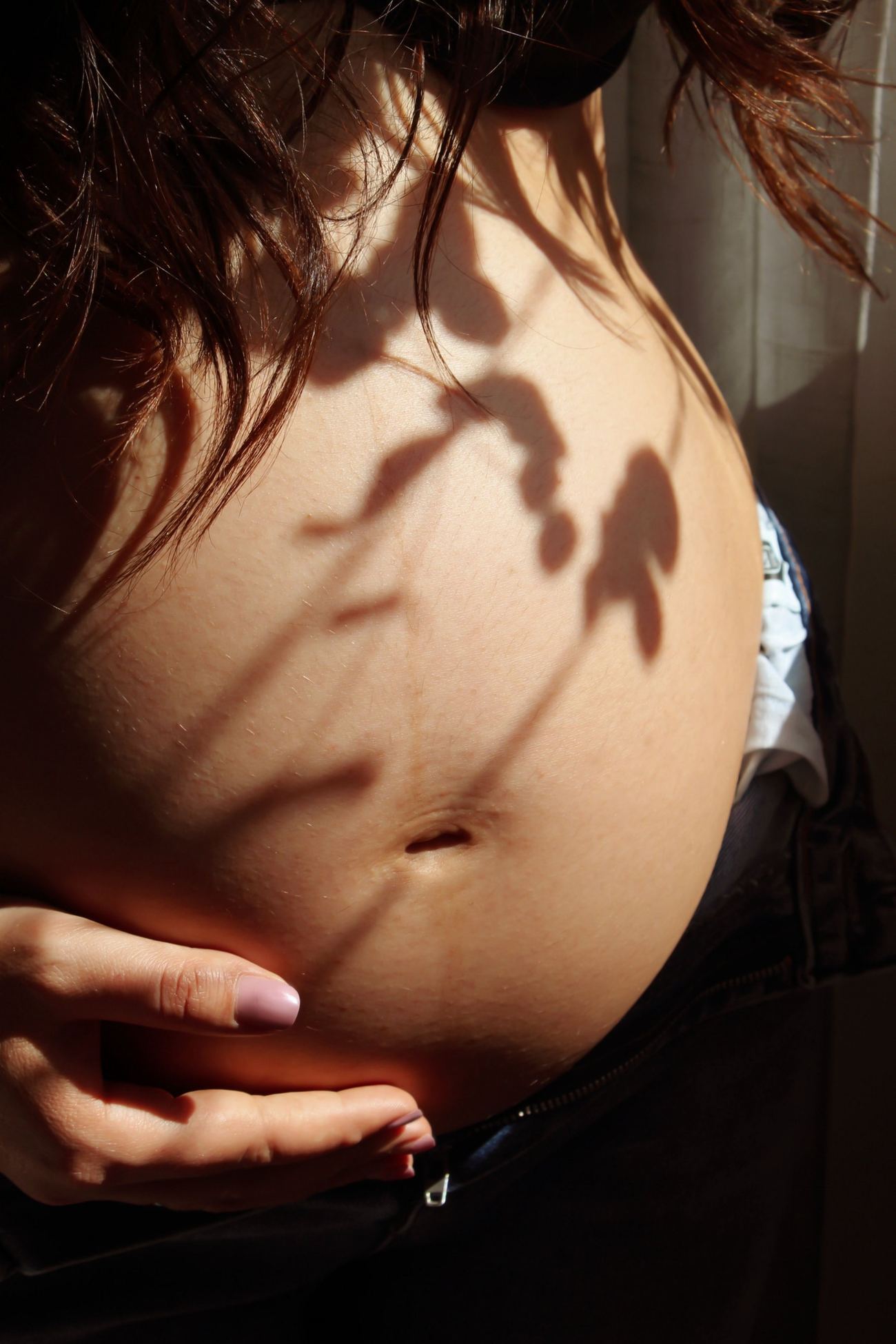 A pregnant woman's bump in dappled sunlight