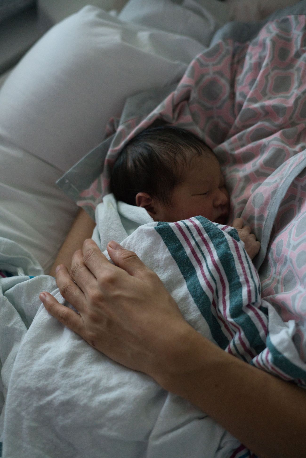 A mother's hand resting on her sleeping newborn