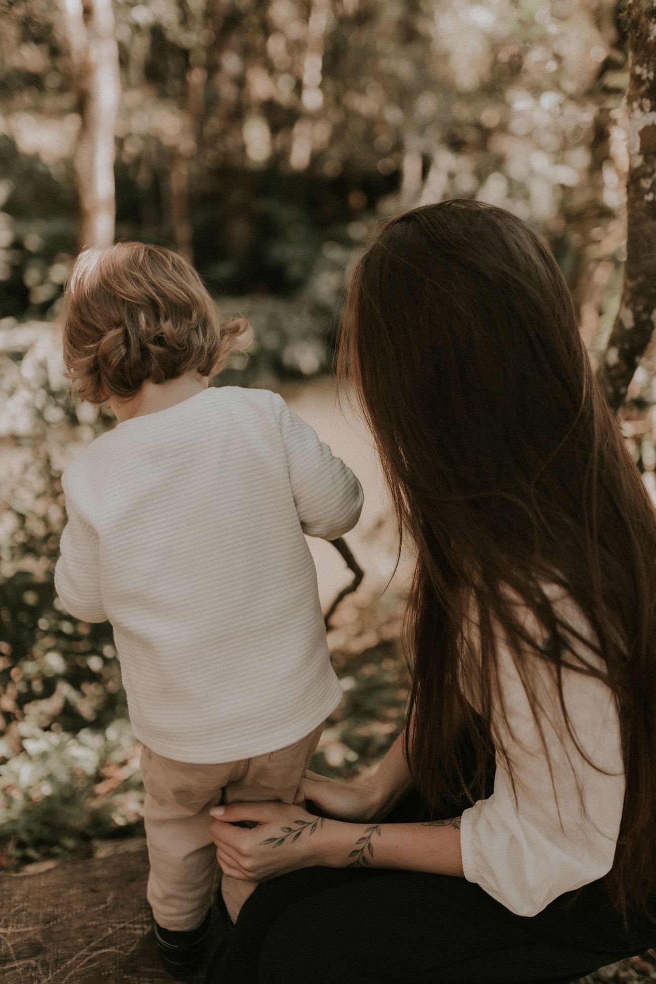 A mother crouched beside her toddler in the woods